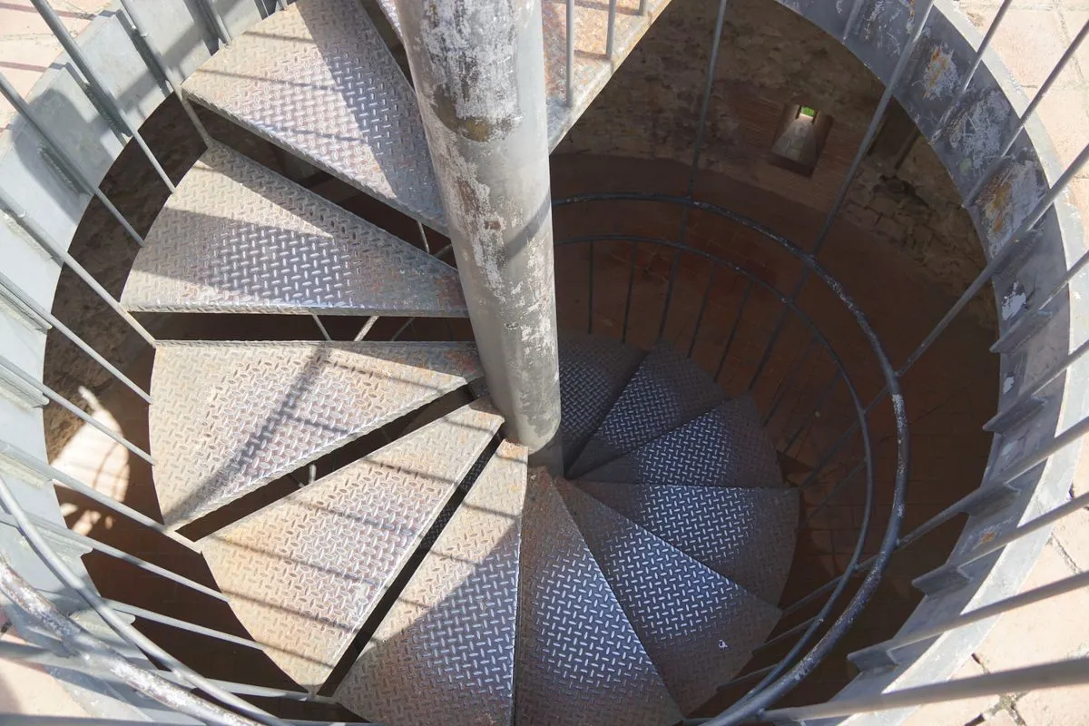 Escada caracol de ferro instalada em mezanino com corrimão metálico